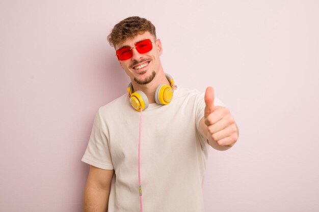 Giovane uomo cool che si sente orgoglioso di sorridere positivamente con i pollici in su occhiali da sole e cuffie