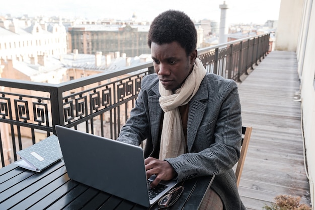 Giovane uomo d'affari africano che lavora online sul laptop mentre è seduto al tavolo in un caffè all'aperto