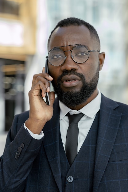 Giovane uomo d'affari africano contemporaneo che tiene smartphone a orecchio