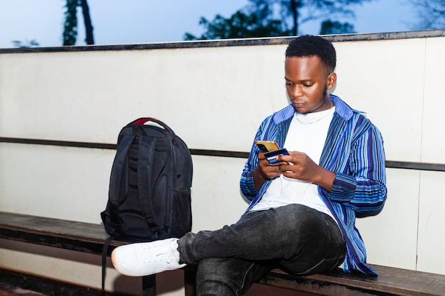 Giovane uomo d'affari africano nero che si trova e utilizza lo smartphone in una stazione degli autobus
