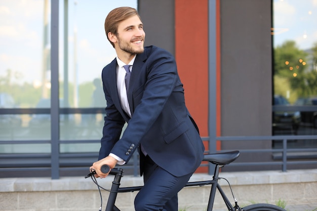 Giovane uomo d'affari alla moda vestito in tuta in sella a una bicicletta su una strada cittadina.