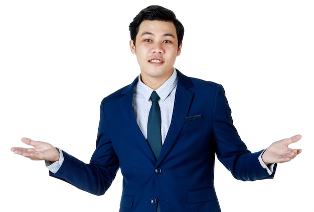 Giovane uomo d'affari asiatico attraente che indossa un abito blu navy con camicia bianca e cravatta che sorride e sembra confuso mettendo le mani di lato. Sfondo bianco. Isolato