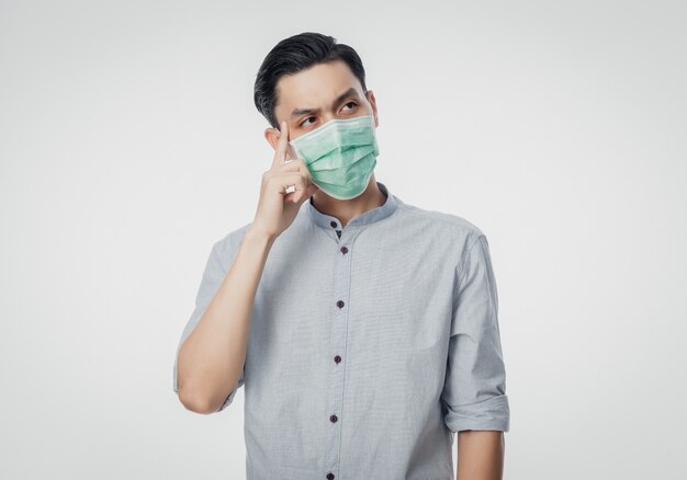 Giovane uomo d'affari asiatico che indossa una maschera igienica e pensando di prevenire l'infezione, 2019-nCoV o coronavirus. Malattia respiratoria dispersa nell'aria come il combattimento con PM 2.5 e influenza isolata sul muro bianco