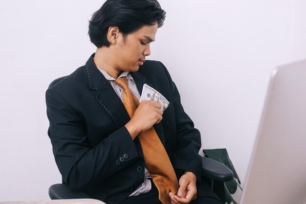 Giovane uomo d'affari asiatico che mette banconote da un dollaro nella sua tuta da tasca in ufficio