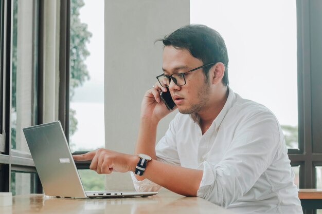 Giovane uomo d'affari asiatico che parla su uno smartphone a una scrivania al caffè