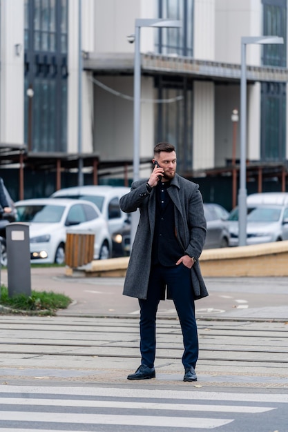 Giovane uomo d'affari attraente ha una telefonata su una strada moderna Uomo alla moda in panno casual che cammina per strada