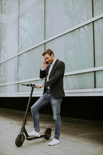 Giovane uomo d'affari bello che utilizza il telefono cellulare su scooter elettrico