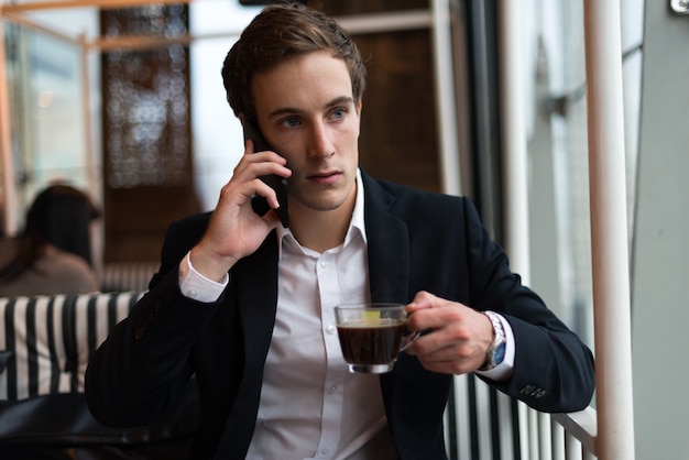 Giovane uomo d'affari bello con caffè parlando al telefono presso la caffetteria