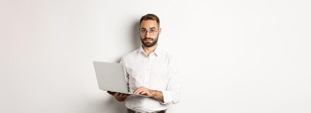 Giovane uomo d'affari bello di affari che lavora al computer portatile facendo il lavoro sul computer che sta sopra la parte posteriore bianca