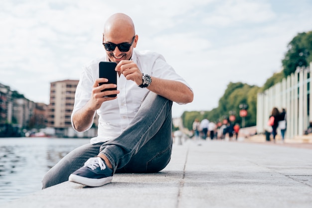 Giovane uomo d&#39;affari bello in una camicia bianca messa da acqua facendo uso dello smartphone