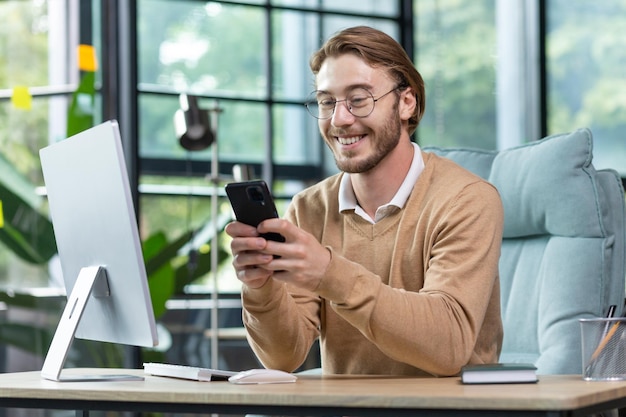 Giovane uomo d'affari bello libero professionista si siede in ufficio al computer e utilizza il tipo di telefono