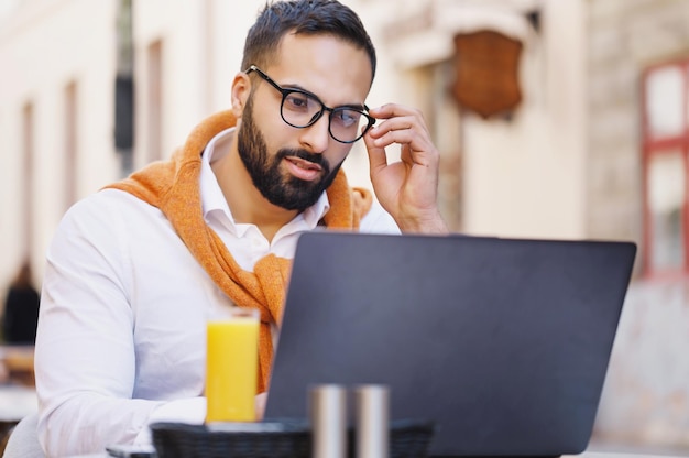 Giovane uomo d'affari bello serio che lavora con il computer portatile mentre beve il succo nella caffetteria all'aperto