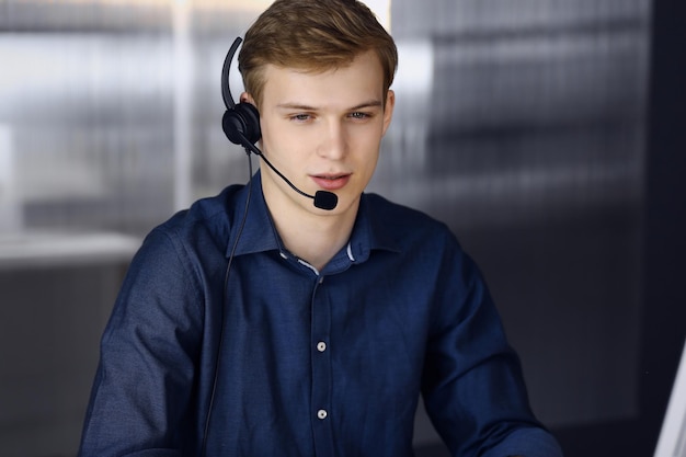 Giovane uomo d'affari biondo che utilizza auricolare e computer al lavoro. Avviare un'attività significa lavorare sodo e fuori tempo per raggiungere il successo.