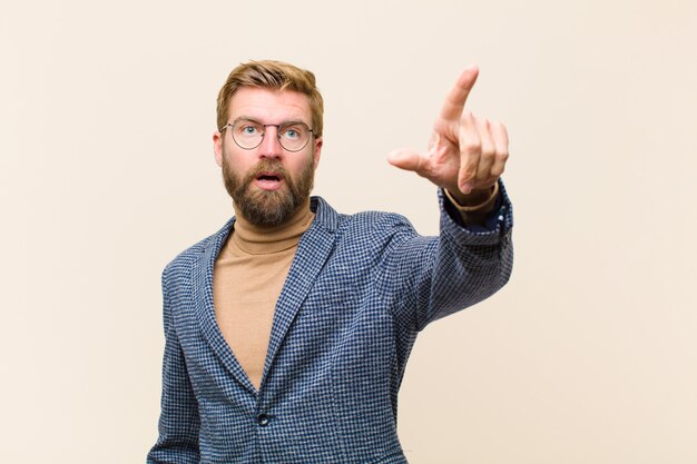 Giovane uomo d'affari biondo sentirsi scioccato e sorpreso, indicando e guardando verso l'alto in soggezione con lo sguardo stupito e a bocca aperta