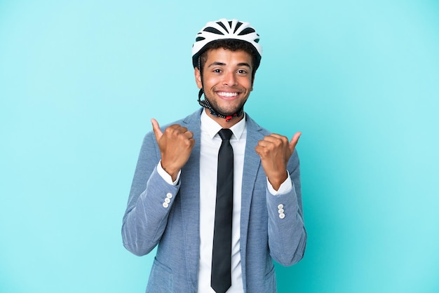 Giovane uomo d'affari brasiliano con casco da bici isolato su sfondo blu con pollice in alto gesto e sorridente