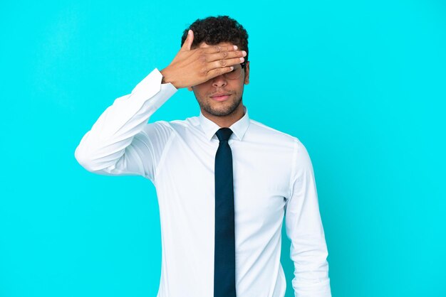 Giovane uomo d'affari brasiliano isolato su sfondo blu che copre gli occhi con le mani. Non voglio vedere qualcosa