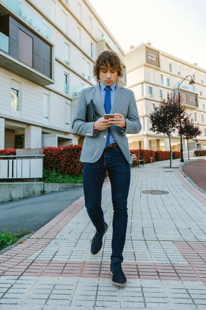 Giovane uomo d'affari che cammina per strada mentre guarda il telefono cellulare