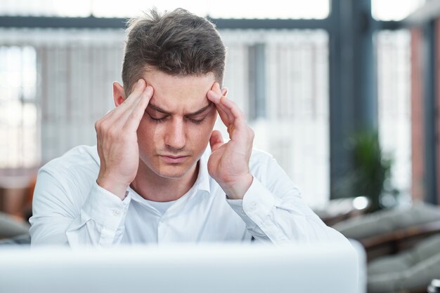 Giovane uomo d'affari che ha mal di testa dopo aver lavorato al laptop tutto il giorno