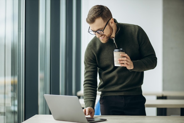 Giovane uomo d'affari che lavora al computer e beve caffè in ufficio