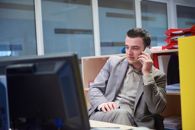 giovane uomo d'affari che lavora al computer e parla al telefono in un ufficio moderno al chiuso