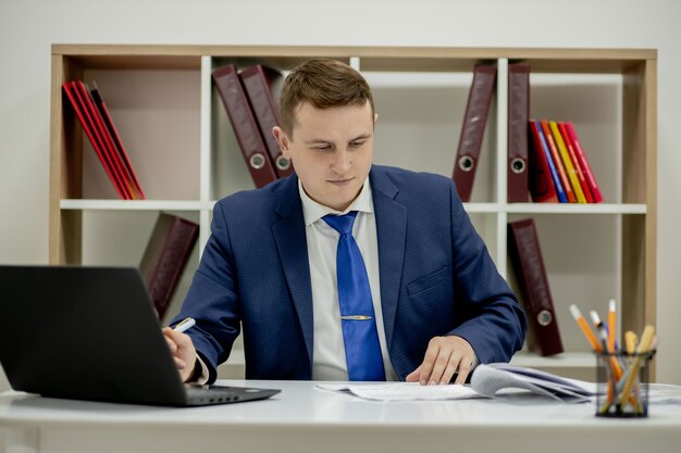Giovane uomo d'affari che lavora con i documenti guardando i documenti nella cartella, seduto alla scrivania dell'ufficio.