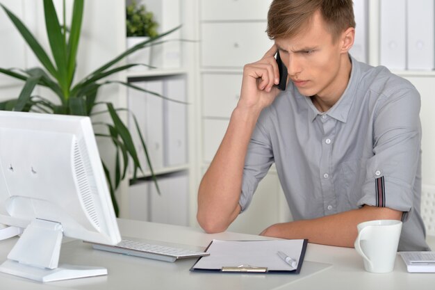 giovane uomo d'affari che lavora in ufficio alla scrivania con computer e telefono