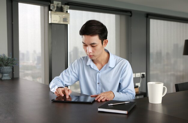 Giovane uomo d&#39;affari che si siede al tavolo sul posto di lavoro in ufficio utilizzando il tablet