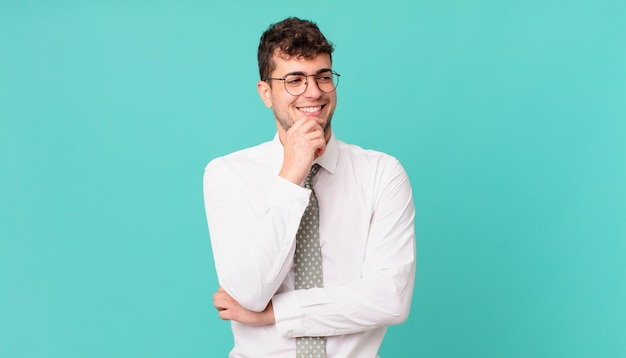 Giovane uomo d'affari che sorride con un'espressione felice e sicura con la mano sul mento, chiedendosi e guardando di lato