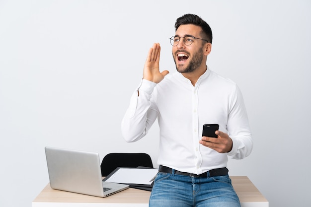 Giovane uomo d'affari che tiene un telefono cellulare che grida con la bocca spalancata