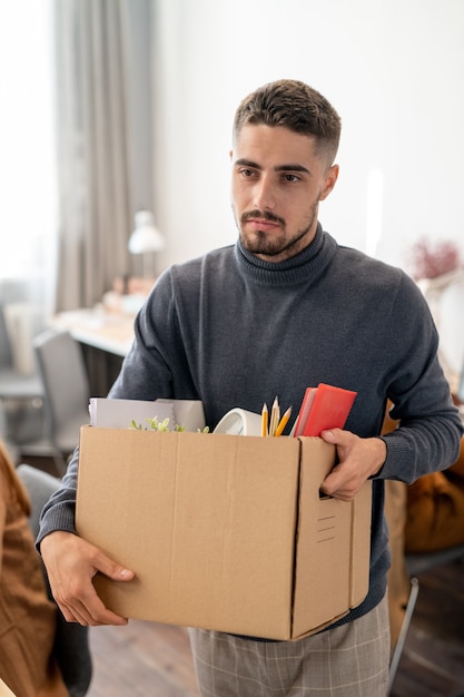 Giovane uomo d'affari che trasporta una scatola con forniture mentre cambia posto di lavoro