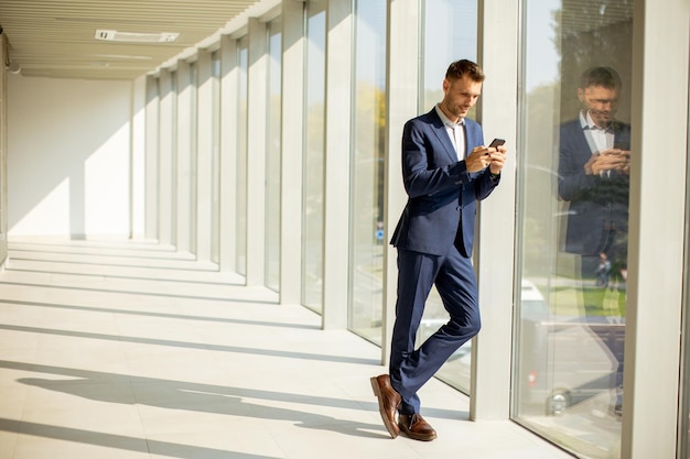 Giovane uomo d'affari che utilizza il telefono cellulare nel moderno corridoio dell'ufficio