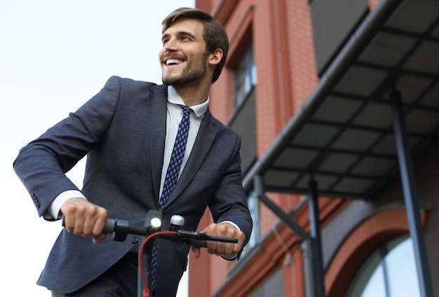 Giovane uomo d'affari che utilizza scooter elettrico sulla strada della città. Concetto di trasporto moderno ed ecologico.