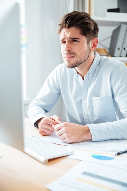 Giovane uomo d'affari concentrato che si siede e lavora con il computer in ufficio