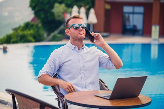 Giovane uomo d'affari di sesso maschile con laptop seduto a bordo piscina Open workplace Concetto di libero professionista Shopping online Lavoro di vacanza