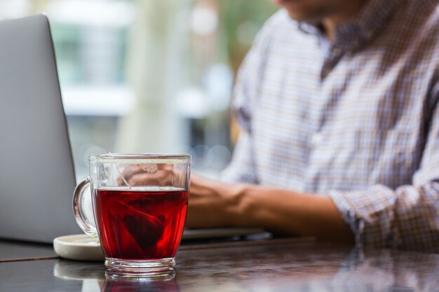 Giovane uomo d'affari di successo seduto in un bar, bevendo tè rosso sano e lavorando su un laptop. Composizione lifestyle con luce naturale