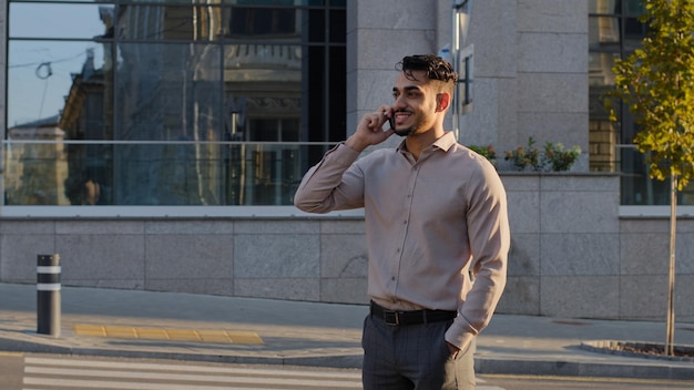 Giovane uomo d'affari di successo sorridente felice barbuto ragazzo capo capo manager si trova in città sulla strada parlando al telefono cellulare rispondendo alla chiamata trattative remote conversazione utilizzando smartphone all'aperto