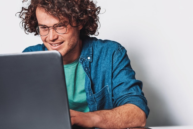 Giovane uomo d'affari felice con i capelli ricci, lavorando sul suo computer portatile in ufficio Sorridente libero professionista uomo seduto alla sua scrivania, navigare in internet sul computer portatile