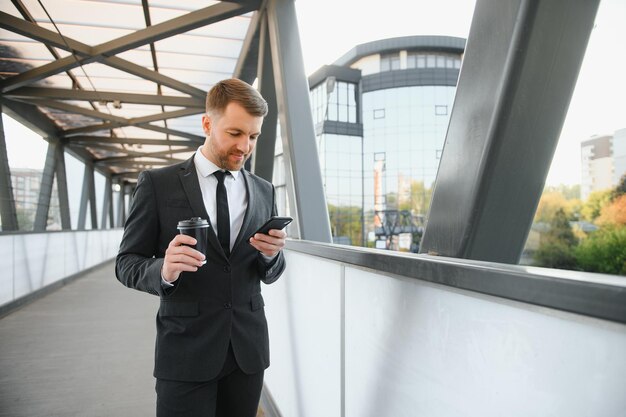 Giovane uomo d'affari fiducioso che utilizza il telefono cellulare e beve caffè in città