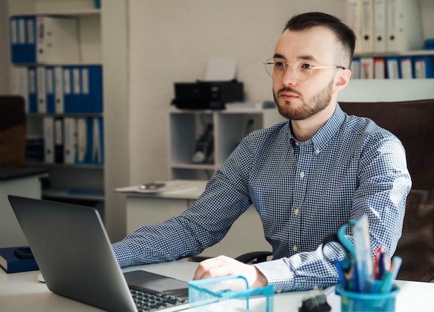 Giovane uomo d'affari in camicia che lavora al suo computer portatile in un ufficio