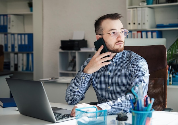 Giovane uomo d'affari in camicia che lavora al suo computer portatile in un ufficio