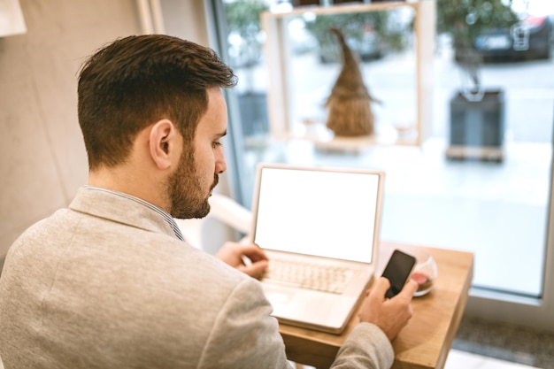 Giovane uomo d'affari in pausa in un caffè. Sta lavorando al laptop e utilizza lo smartphone.