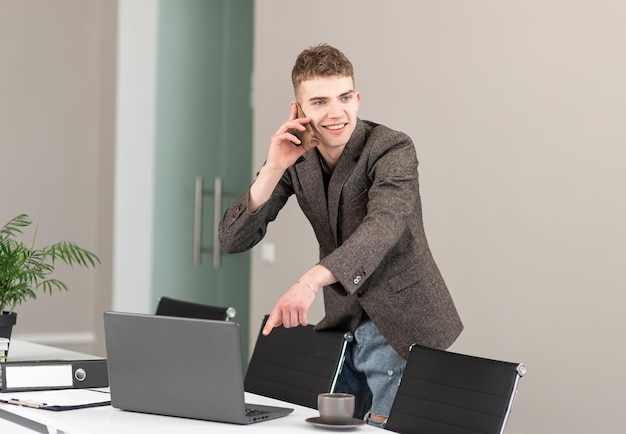 Giovane uomo d'affari in piedi in un ufficio moderno e parlando al telefono