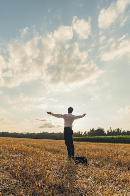 Giovane uomo d'affari in piedi nel mezzo di un campo segato sotto un bel cielo con le braccia allargate.