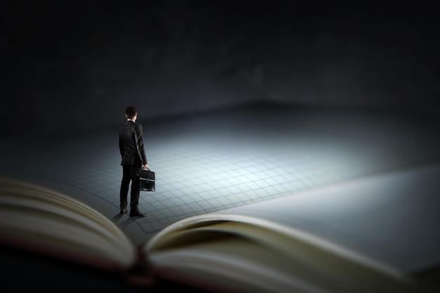 Giovane uomo d'affari in piedi su un libro enorme. Tecnica mista