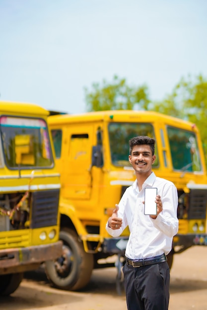 Giovane uomo d'affari indiano con il suo camion o camion e mostrando lo smartphone.