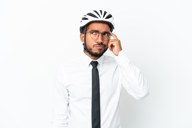 Giovane uomo d'affari latino che tiene un casco da bici isolato su sfondo bianco con dubbi e con espressione faccia confusa