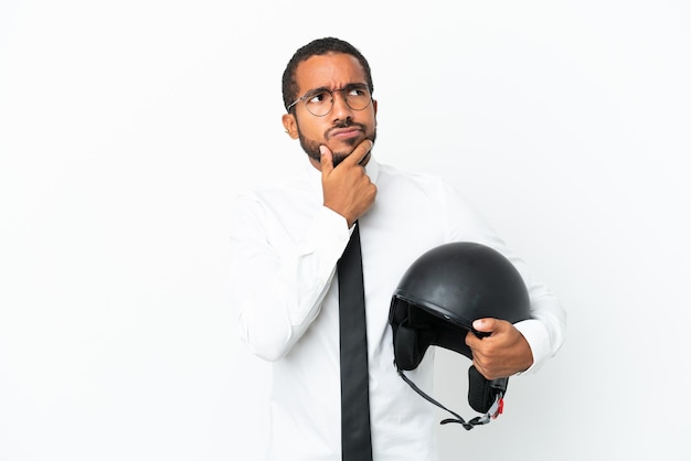Giovane uomo d'affari latino con un casco da motociclista isolato su sfondo bianco con dubbi