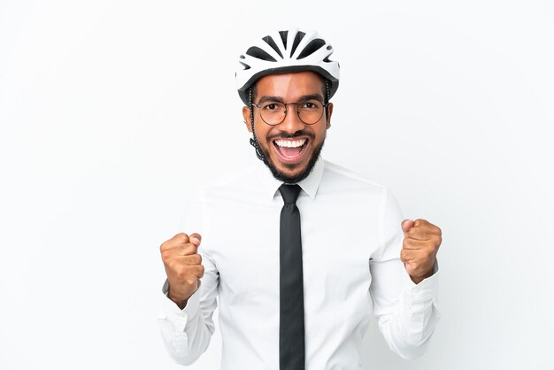 Giovane uomo d'affari latino in possesso di un casco da bici isolato su sfondo bianco che celebra una vittoria in posizione di vincitore