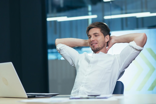 Giovane uomo d'affari libero professionista manager in ufficio al tavolo che riposa facendo il lavoro durante una pausa gettando le mani dietro la testa sorridendo