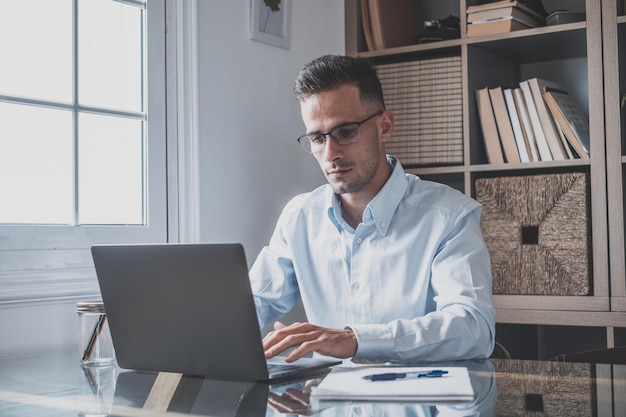 Giovane uomo d'affari millenario caucasico felice che lavora a casa alla scrivania con il portatile o il computer che si diverte Giovane uomo in videoconferenza che si occupa dell'attività o del mercato